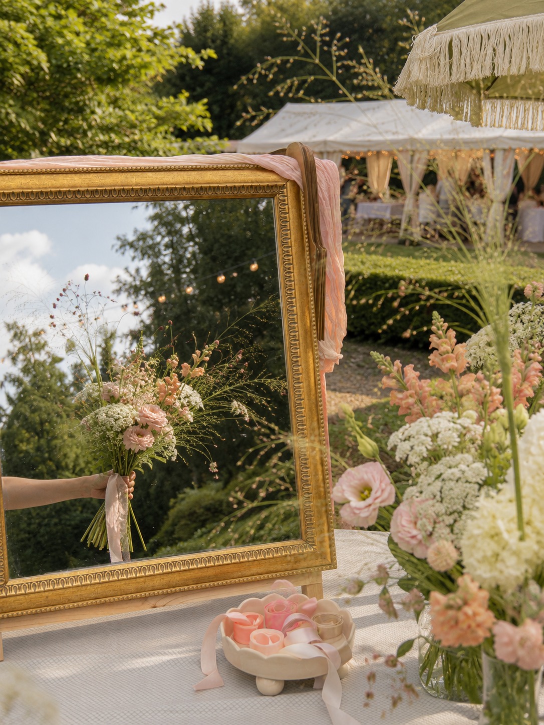 Gast houdt zelfgemaakt boeket vast voor gouden spiegel bij bloemenbar tijdens buitenevenement